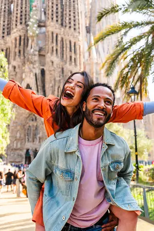 A couple smiling in front of the Sagrada Familia cathedral in Barcelona, Spain