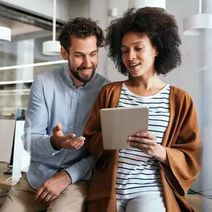 A man and a woman sitting and looking at a tablet together in an office