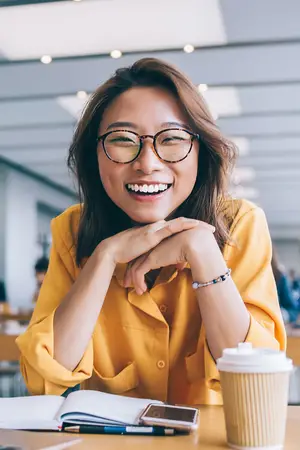 Close up of a smiling woman in a yellow shirt sitting at a table with a book and a cup of coffee