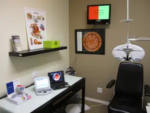 An indoor room with a desk and medical equipment such as an eye exam chair and a monitor mounted on the wall.