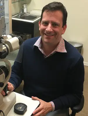 A man is smiling and looking through a microscope inside a laboratory.