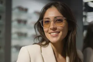 A smiling woman wearing glasses and a white suit jacket.