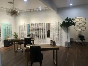 Interior of an optometrist's office with wooden flooring, white walls, a chandelier, desks, and a potted plant.