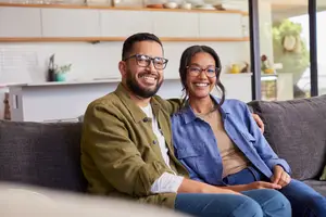 Smiling couple sitting on a sofa in a modern living room with a kitchen background.