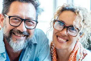 A man and a woman are smiling and wearing glasses