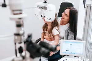 A young girl is having her eyes examined by an adult woman in a clinic.