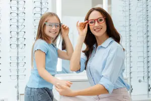 A woman and a girl are trying on glasses in front of a mirror at an optometrist's office.