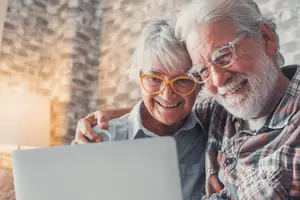 An elderly couple using a laptop with a smiling expression
