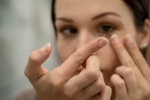 A woman is examining a contact lens on her fingertip.