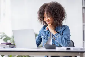 Woman smiling while sitting at a desk with a laptop and books in front of her