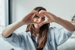 woman making a heart shape with her hands and smiling