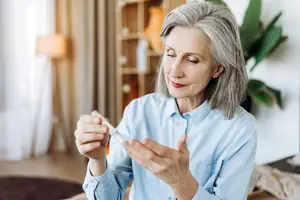 An older woman is sitting on a couch in a living room and holding a bottle in her hand.