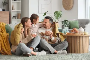 A family of three sitting on a couch with cups of coffee and smiling.