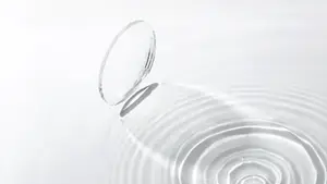 A clear circular contact lens is resting on a rippled water surface.
