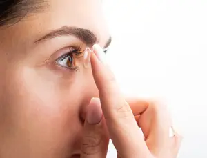 A close-up of a woman wearing a ring and adjusting her contact lens with her finger