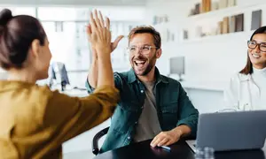Three people are smiling and giving high fives in an office room.