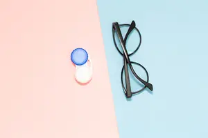 A pair of glasses and a blue contact lens case on a blue and pink background