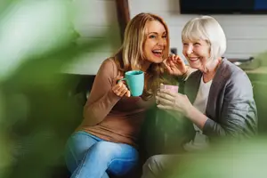 Two women sitting on a couch, one holding a cup and smiling, and the other woman smiling and looking at the cup