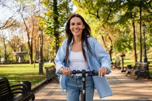 A smiling woman riding an electric scooter in a park with benches and trees