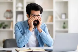 Tired man rubbing his eyes while sitting in his home office