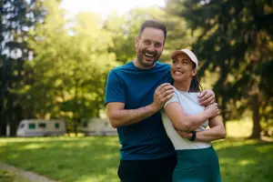 A couple standing outside in a grassy area with trees and a camper in the background