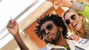 A man and a woman are posing for a picture with one of them holding a cigarette and the other holding a drink