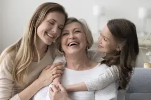 Three women smiling and embracing each other on a couch