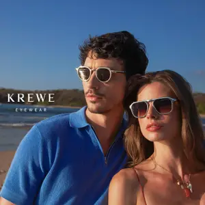 A man and a woman are standing on a beach wearing sunglasses and smiling for a photo.