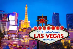 A neon sign for Las Vegas, Nevada, is displayed in front of a cityscape at night, featuring a large sign with the words 'Welcome to Fabulous Las Vegas, Nevada' illuminated and surrounded by buildings and a tower.