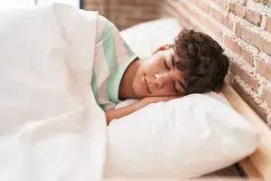 A boy sleeping on a bed with his head resting on a pillow and his eyes closed