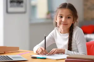 A young girl is sitting at a desk and writing in a notebook.