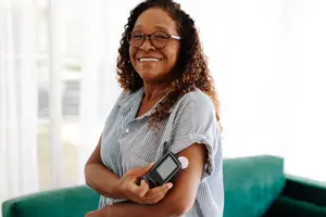 A smiling woman wearing glasses and holding a device to check her blood sugar.