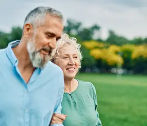 An older couple standing in a park with yellow flowers in the background