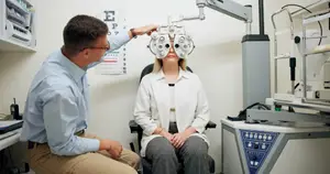 A man and woman are sitting in a doctor's office with an eye exam machine