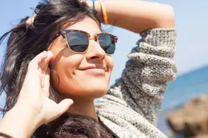 A woman wearing sunglasses is smiling and posing for a photo on the beach.