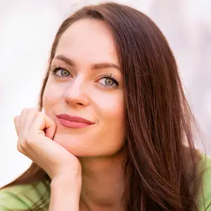 A smiling woman with brown hair and pink lipstick is posing for a photo.