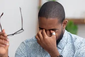 Man holding glasses while rubbing his eye with his hand