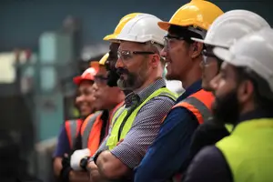 Workers in safety gear stand in a line inside a factory.