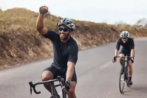 Two men cycling on a road with one man raising his fist in victory
