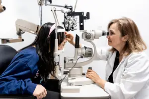 A woman is having her eyes examined by a doctor in a white coat using a machine