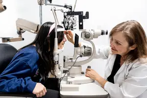 A female optometrist is examining the eyes of a young girl with a slit lamp in a clinic.