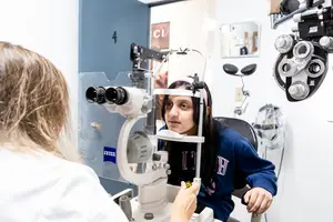 A young girl is getting her eyes examined by a woman in a lab coat in a clinic.