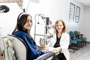 A girl sitting in an eye examination chair with an optometrist beside her in an office