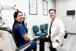 Two medical professionals in an exam room smile for the camera.