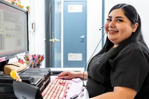 A woman sitting at a desk wearing a headset smiling for the camera