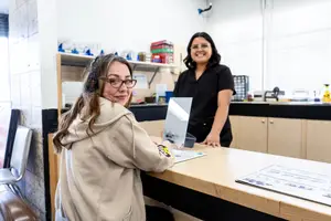 Two women smiling and standing in front of a desk in a room
