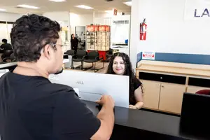 A man and woman stand at a desk in an office with a Dell computer on it.