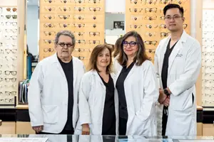 Four individuals in white coats posing for a photograph in front of a wall displaying various glasses frames
