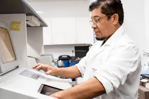 A man wearing glasses and a lab coat is pressing a button on a machine in a laboratory