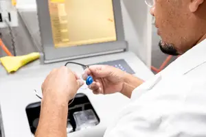 A medical technician is working with a medical device and examining a blue object with a wire